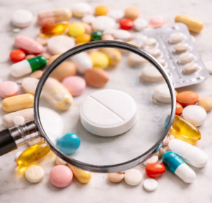 Auf einem Tisch liegen Medikamente, die mit einer Lupe betrachtet werden - Symbolbild zum Thema "Medikationsanalyse"